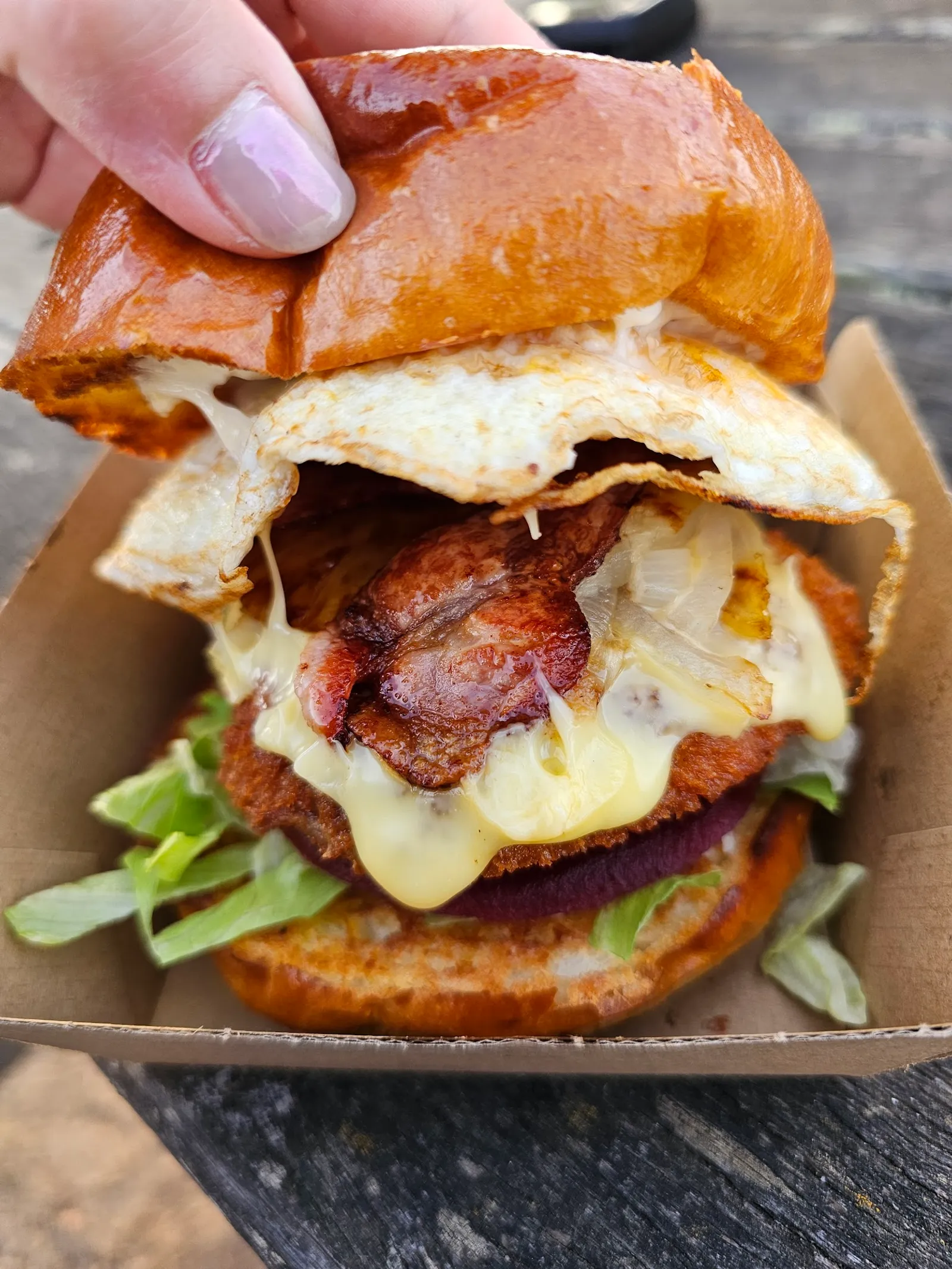 Burger with the lot held open showing egg, bacon, cheese, beetroot and lettuce layers in a cardboard box