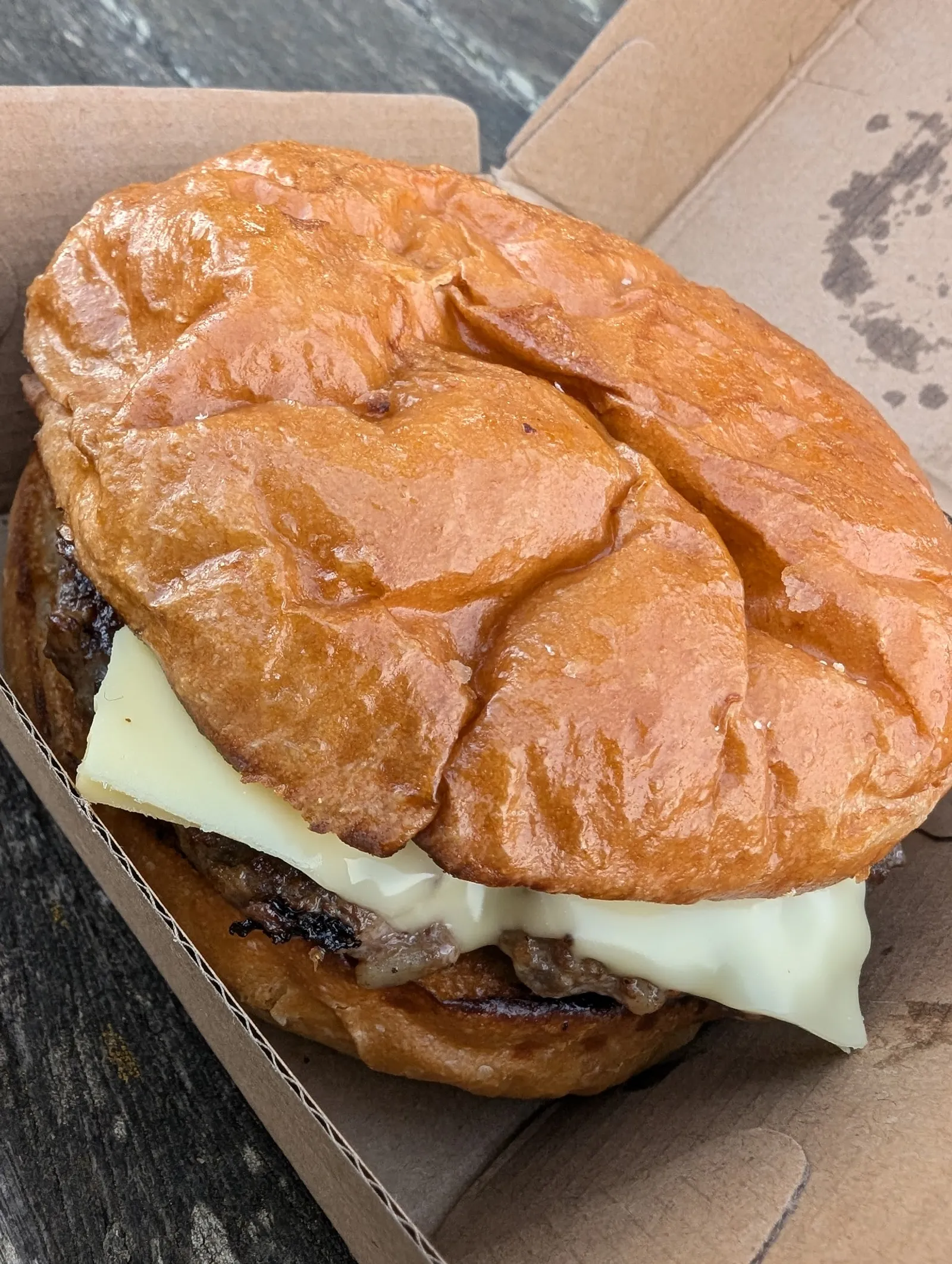 Plain cheeseburger with melted cheese in a cardboard box on a wooden surface, close-up